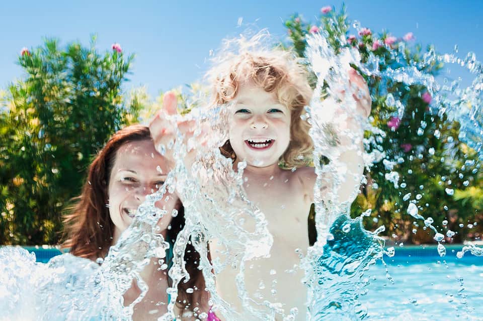 Children splashing in pool with flowering plants and blue sky in background
