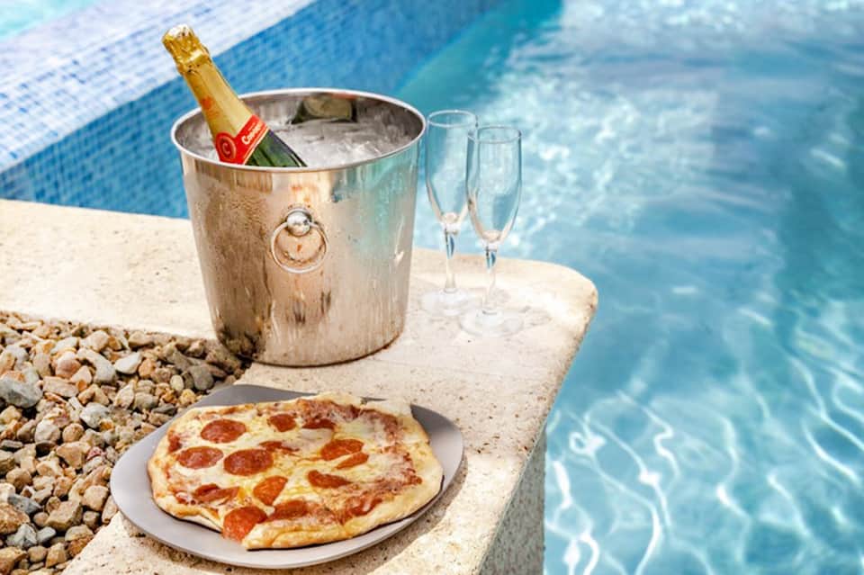 Champagne bucket and pizza on pool deck overlooking turquoise swimming pool water