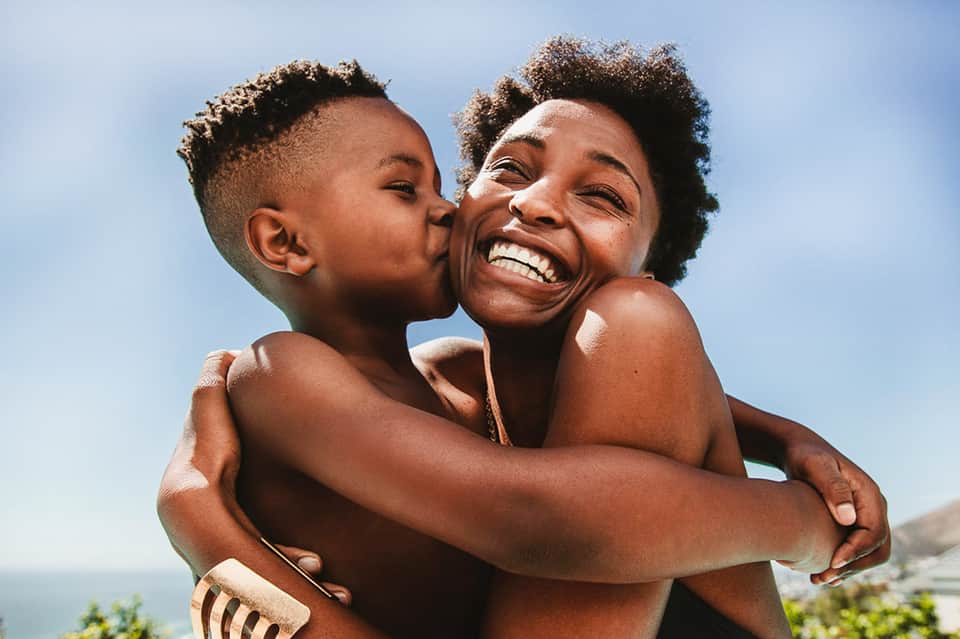 Woman and child hugging outdoors with ocean view in background