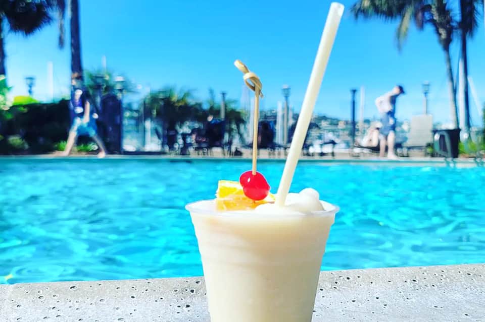 Tropical cocktail with cherry garnish by poolside with palm trees and city skyline in background