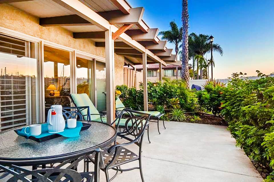 Modern patio with round table, pergola, tropical plants, and city views at sunset
