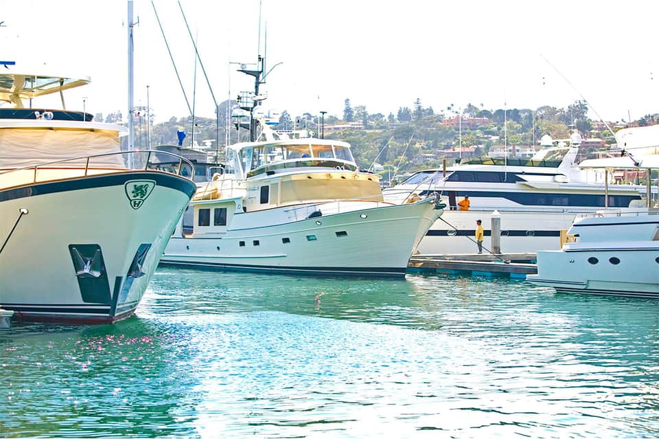 Marina with moored luxury yachts and sailboats in turquoise water with hillside homes