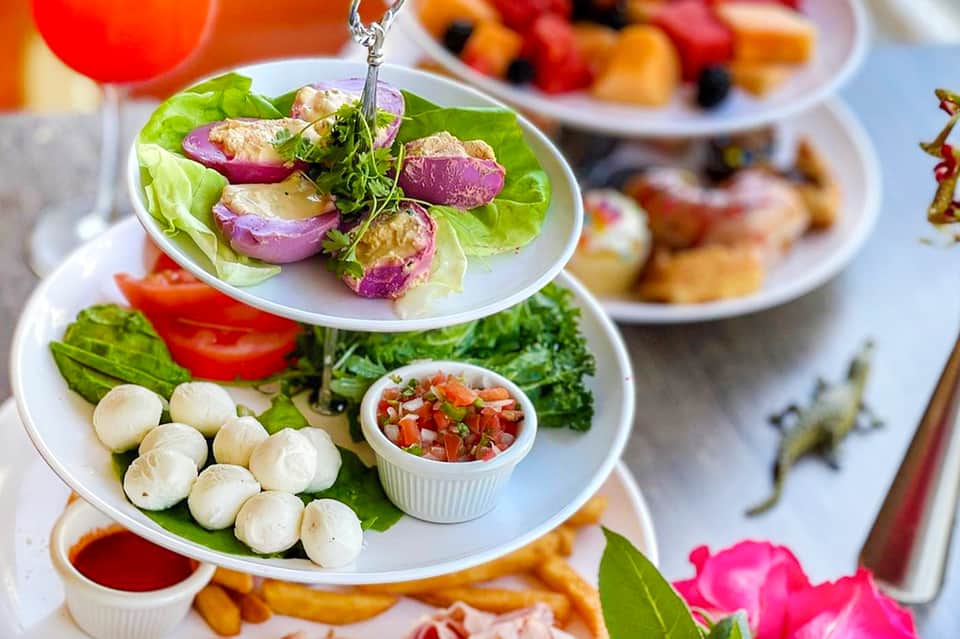 Colorful gourmet appetizers on tiered white plates with beverages and tropical flowers