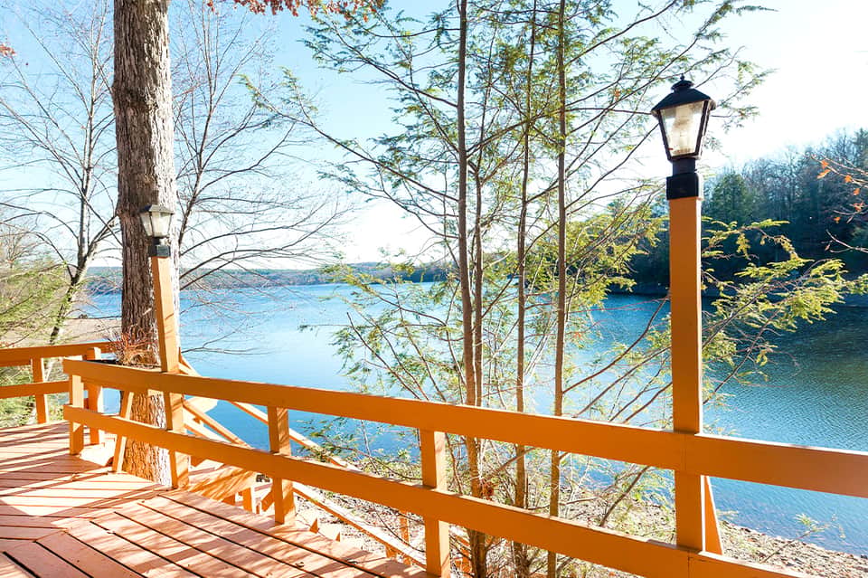 Wooden deck with bench overlooking a serene blue lake surrounded by bare trees and forest landscape