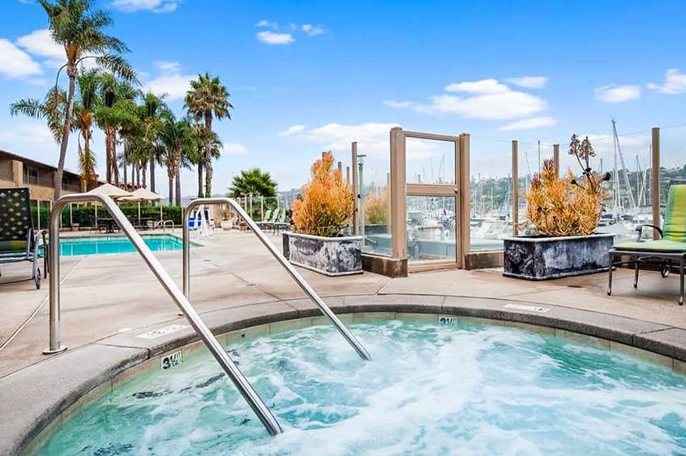 Hot tub with metal railings on waterfront deck overlooking marina with sailboats and palm trees