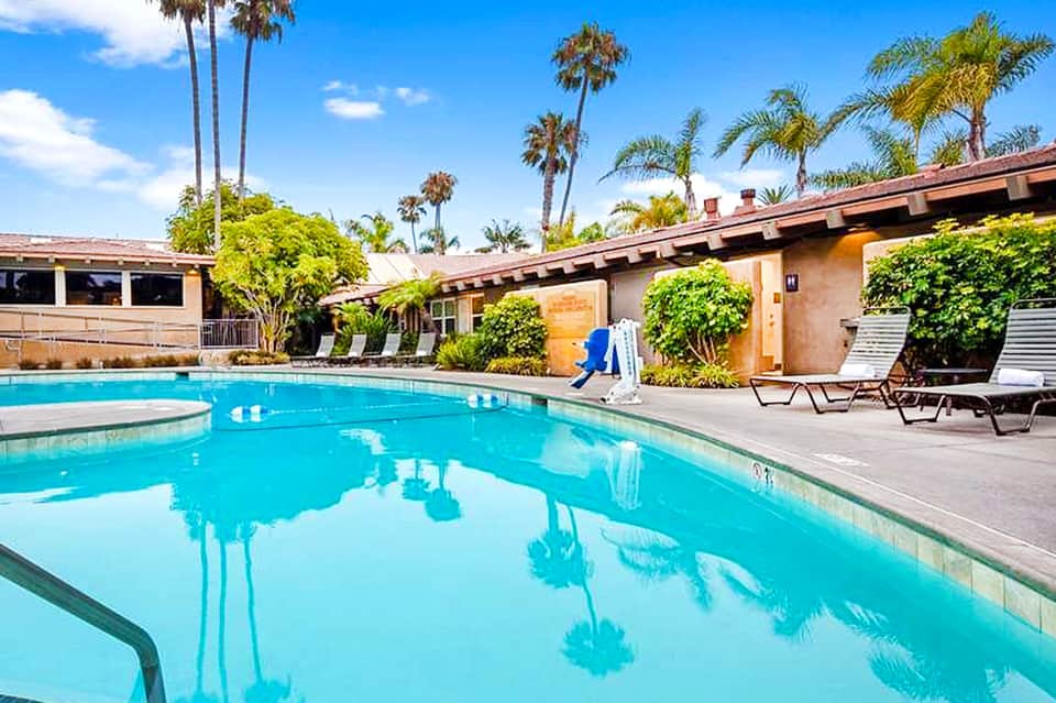 Resort courtyard pool surrounded by palm trees, lounge chairs, and single-story buildings
