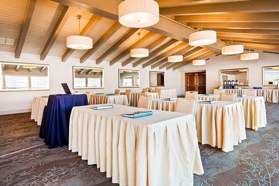 Banquet hall with round tables dressed in cream linens and exposed wood beam ceiling