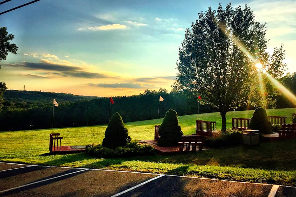 Scenic sunset view over grassy field with flags and benches surrounded by forested landscape