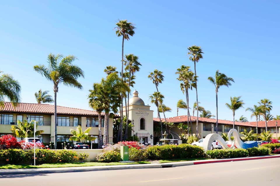Spanish colonial-style resort exterior with palm trees, bell tower, and manicured grounds