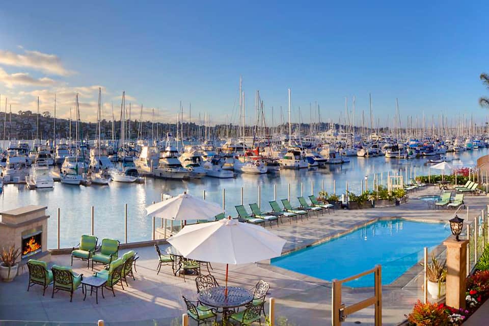 Marina-view pool with sailboats, lounge seating, umbrellas, and waterfront promenade at sunset
