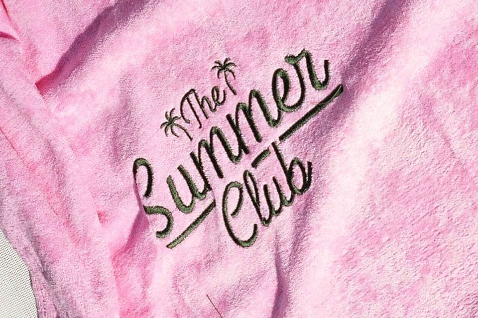 Pink towel embroidered with 'That Summer Club' text with palm tree designs