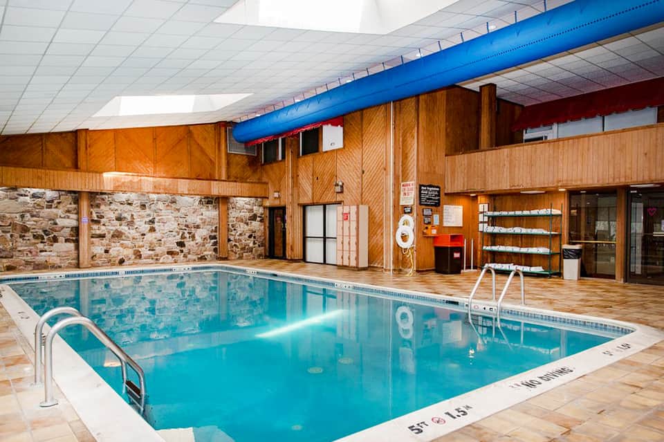 Indoor lap pool with wooden beams, white ceiling, and stone accent walls