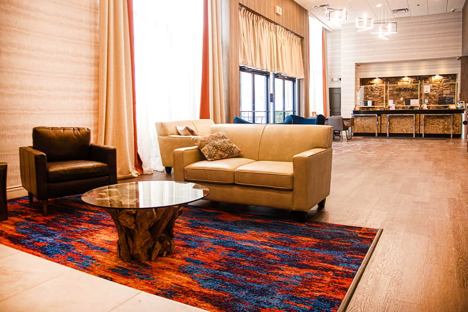 Modern hotel lobby with tan leather seating, colorful rug, and reception desk