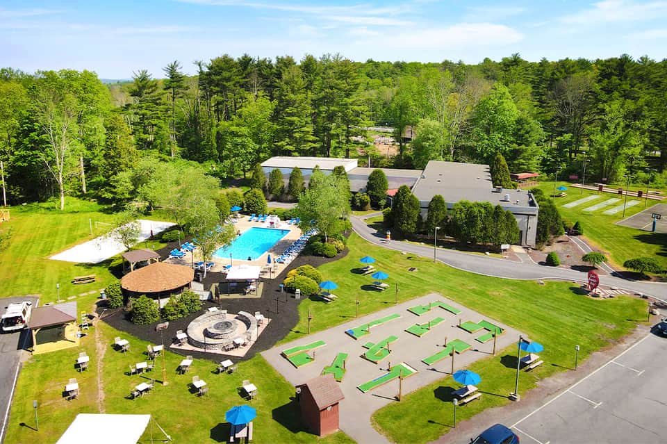 Aerial view of resort pool nestled in wooded grounds with fire pit and mini golf