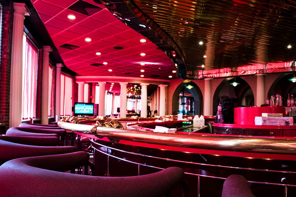 Nightclub interior with pink neon lighting, curved seating, and dance floor