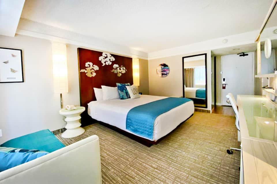 Modern hotel room with king bed, red headboard, blue accent runner, and ensuite bathroom