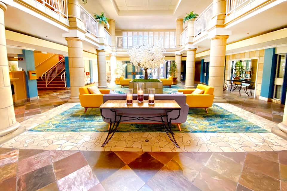 Grand hotel lobby with colorful floor tiles, yellow armchairs, and crystal chandelier under high ceiling