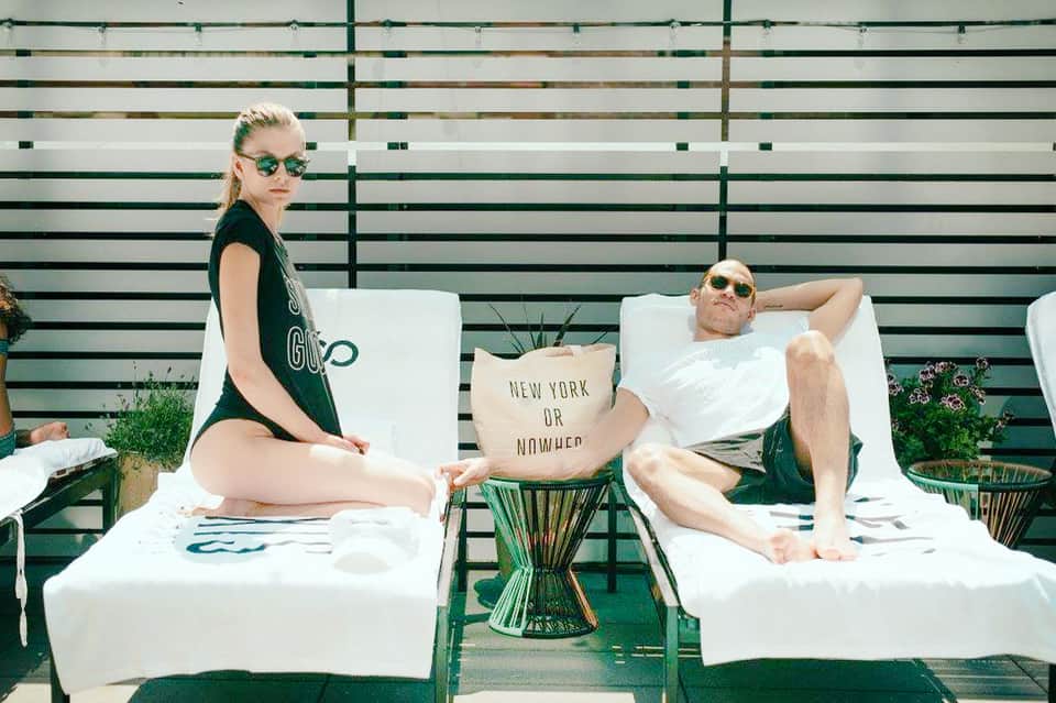 Two guests relaxing on white lounge chairs against a striped green and white backdrop
