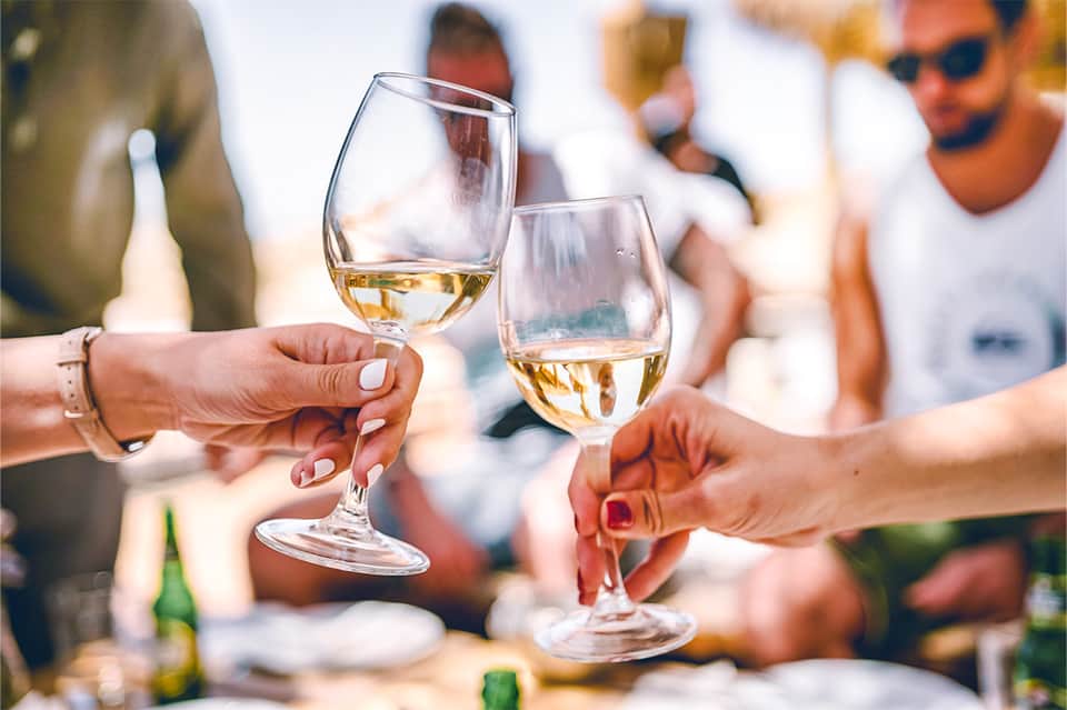 Two people toasting with glasses of white wine at an outdoor seaside gathering
