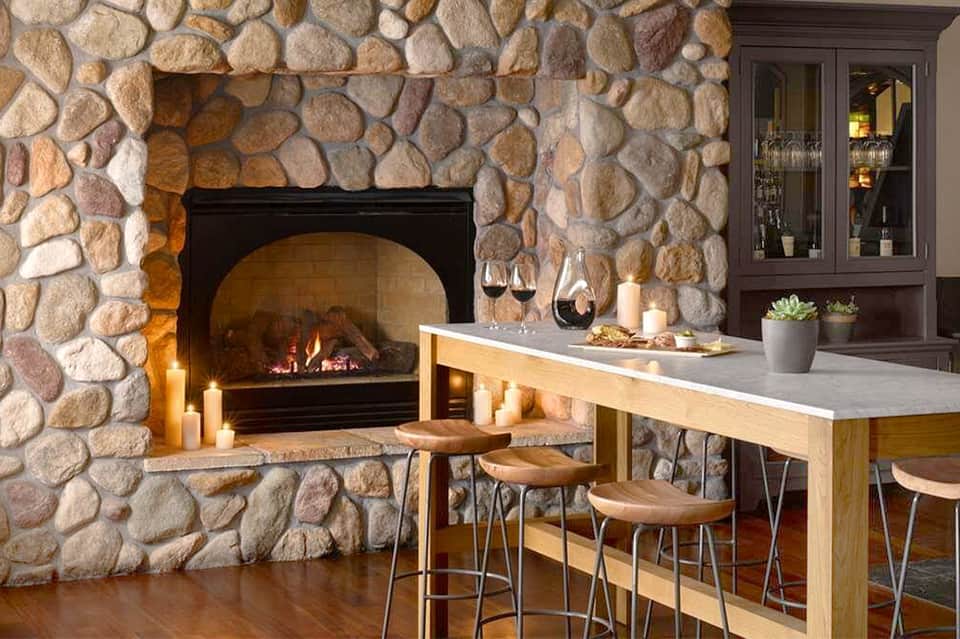 Stone fireplace with crackling fire in modern bar lounge with wine glasses and seating