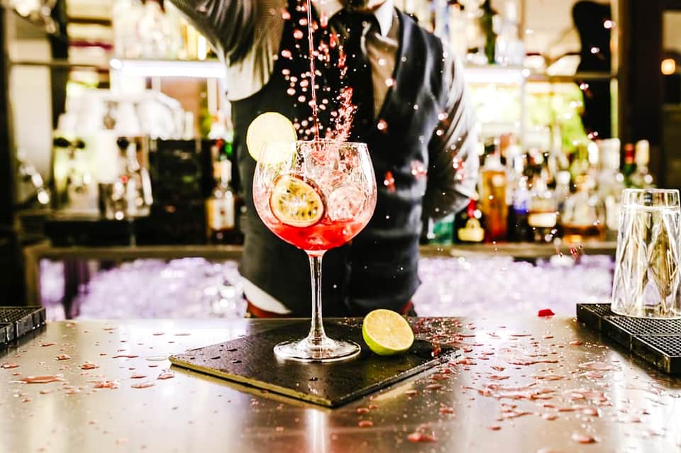 Bartender pouring red cocktail into glass at hotel bar with bottle display