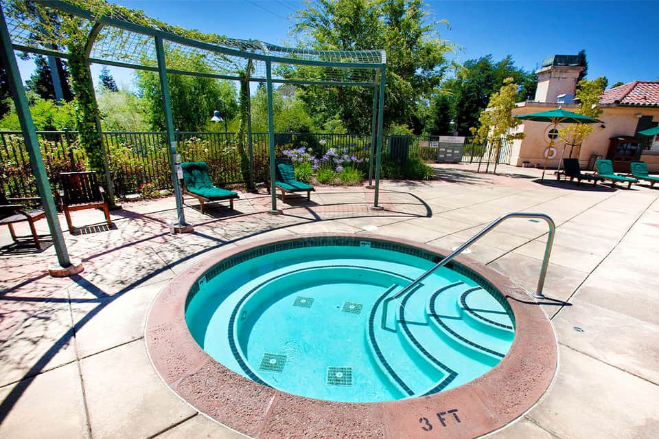 Resort hot tub with spiral design on sunny patio surrounded by lounge chairs and pergolas
