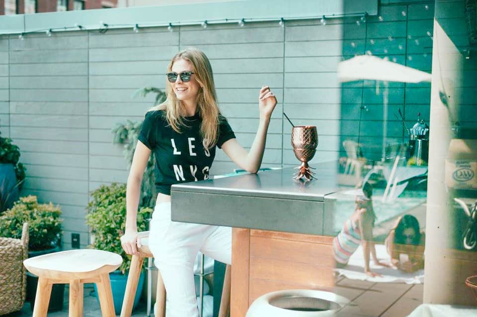 Woman enjoying tropical drink at outdoor rooftop bar with green glass walls and potted plants