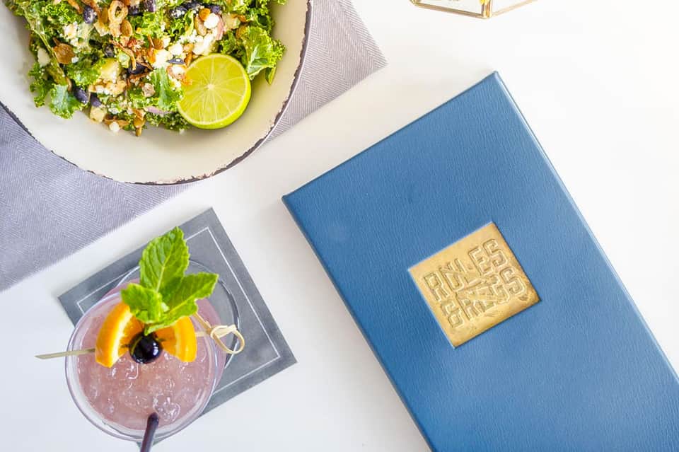 Fine dining salad with lime garnish, cocktail with fruit, and blue resort guide on white surface