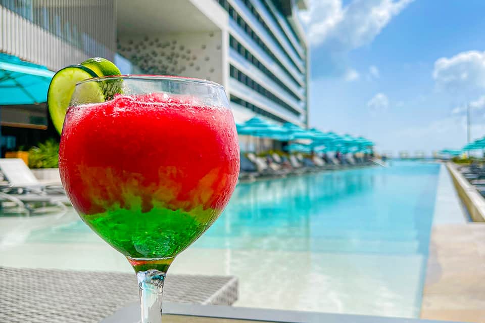 Colorful layered cocktail with lime garnish by resort pool and lounge chairs