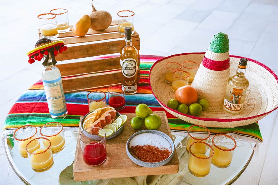 Colorful Mexican-themed party spread with tequila bottles, sombrero, citrus, and cocktails