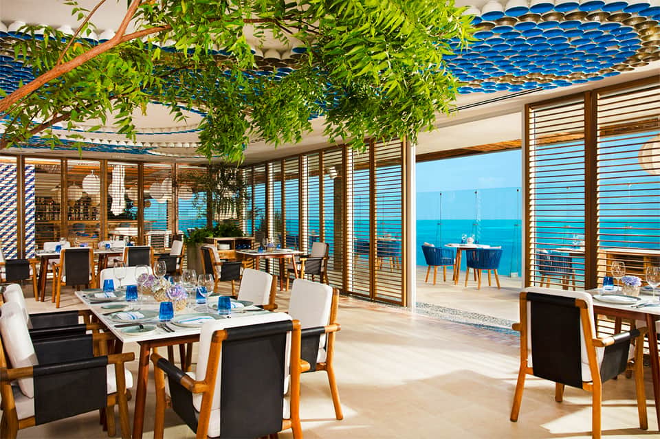 Upscale oceanview restaurant with wooden furnishings, hanging greenery, and blue water vistas