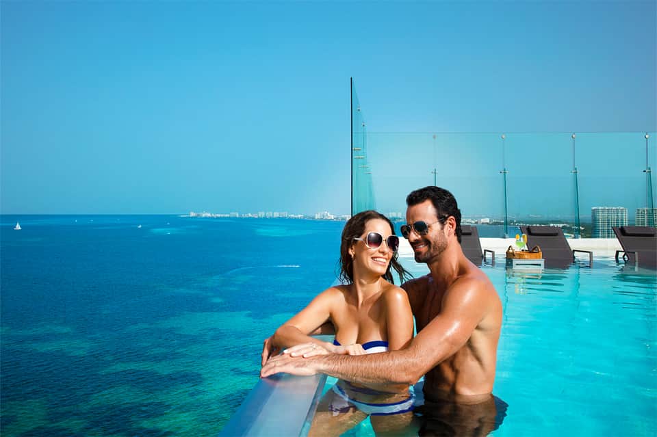 Couple in infinity pool overlooking turquoise ocean and coastal cityscape at luxury resort