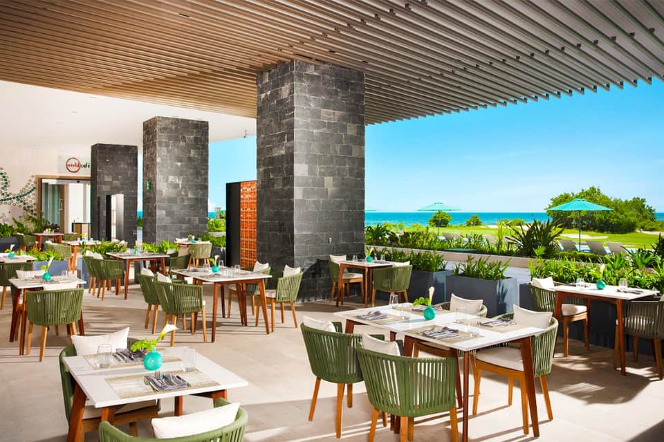 Beachfront restaurant with ocean view, green chairs, wooden tables, and modern architecture pillars