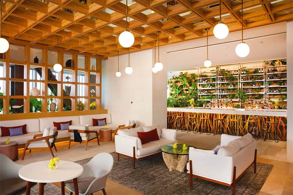 Modern lobby lounge with wooden lattice ceiling, pendant lights, plants, and mid-century furniture