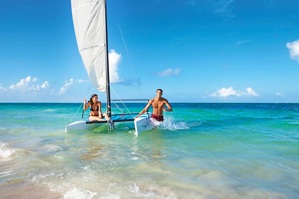 Couple with sailboat in crystal-clear turquoise tropical ocean water