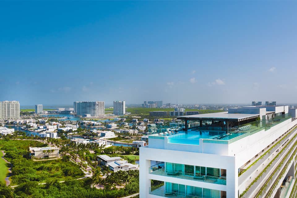 Aerial view of resort with rooftop pool, cityscape, wetlands, and multiple turquoise pools