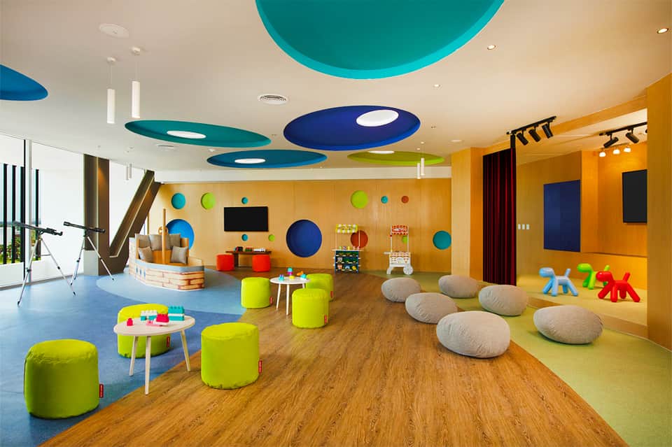 Colorful children's playroom with bright yellow walls, blue ceiling features, soft seating, and interactive toys