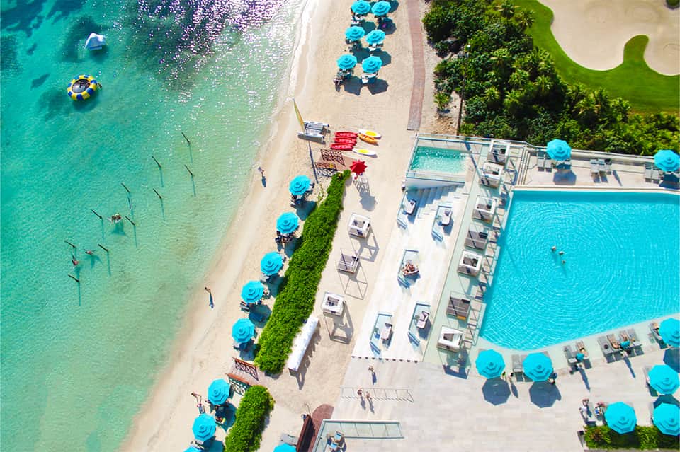 Aerial beach resort view with turquoise umbrellas, pool, ocean access, and manicured landscaping