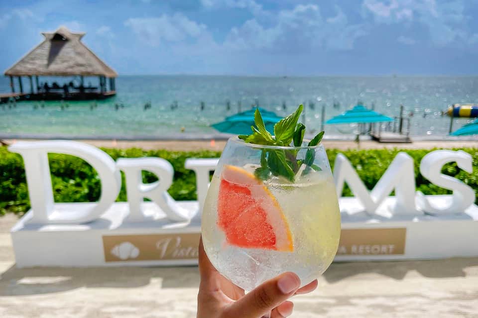 Tropical cocktail with grapefruit and mint garnish overlooking ocean beach cabana and resort sign