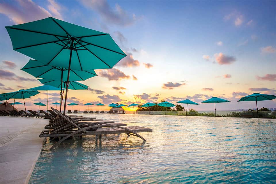 Beachfront lounge at sunset with turquoise umbrellas, dark loungers in shallow water