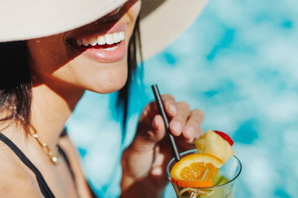 Woman in white hat enjoying tropical cocktail with fruit garnish by pool