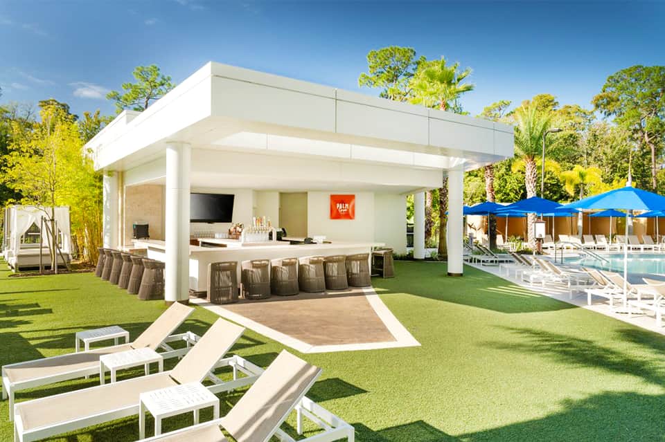 Modern resort bar with white pergola overlooking pool deck and manicured lawn