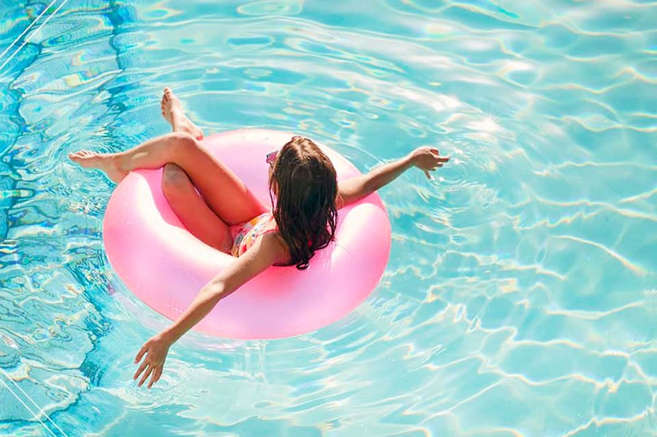 Child floating on pink inflatable ring in crystal clear turquoise swimming pool