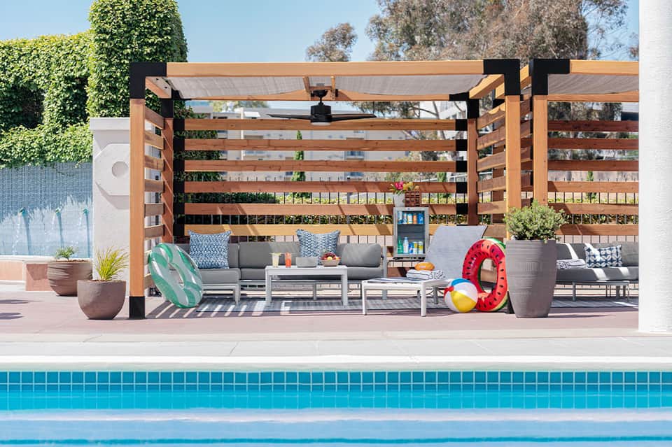 Modern wooden pergola poolside with gray seating and decorative elements
