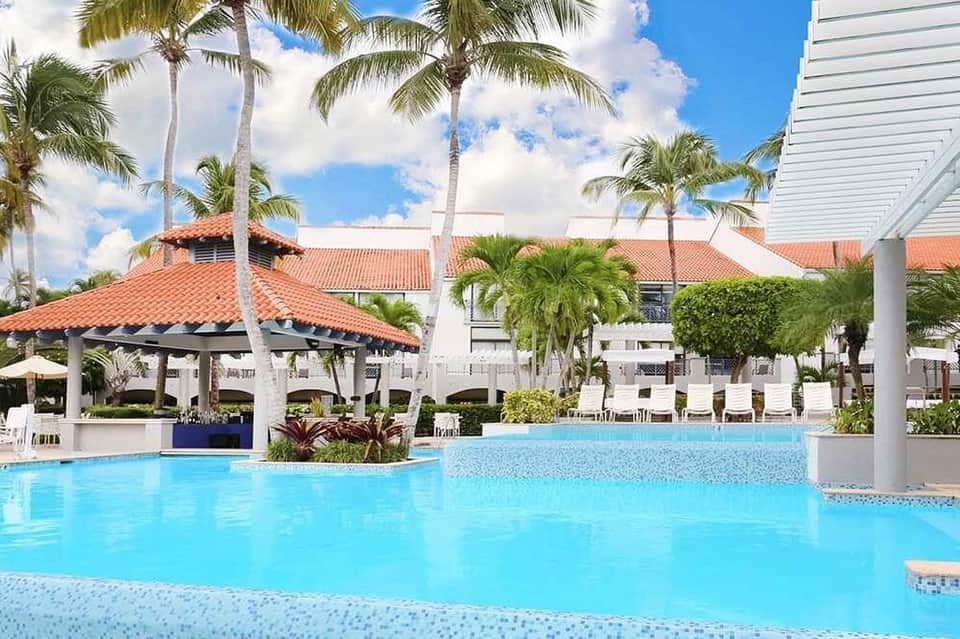 Luxury resort pool with palm trees, Spanish-style architecture, and covered lounge area