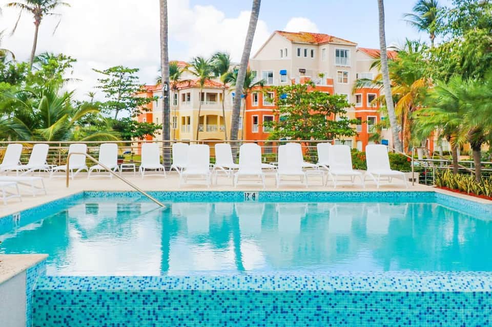 Resort pool with white lounge chairs, colorful buildings, and palm trees