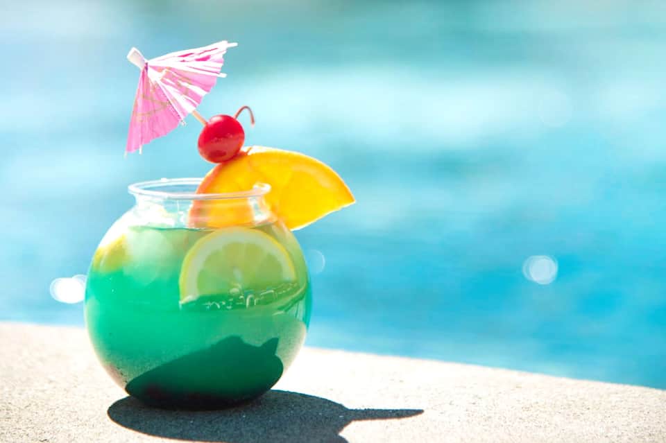 Tropical cocktail with lime slice and pink umbrella on white sand beach with ocean backdrop