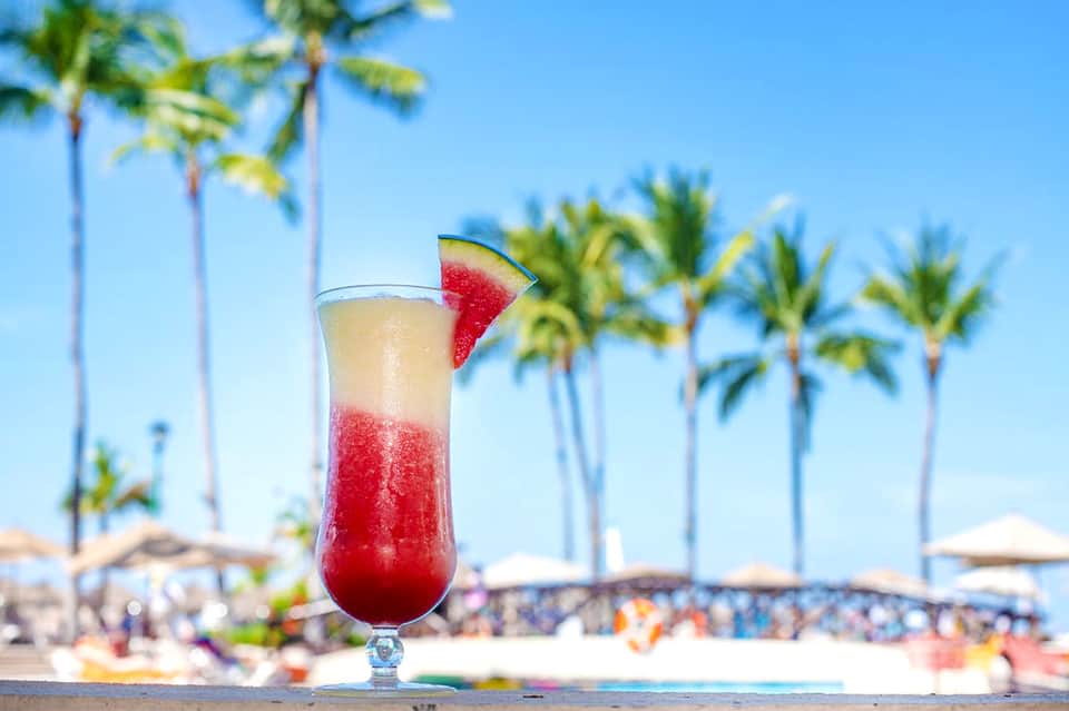 Refreshing red cocktail with watermelon garnish on tropical beach with palm trees