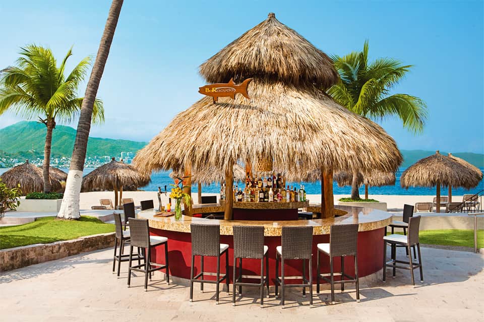Beach bar with thatched roof, palm trees, ocean view, and tiki-style seating area