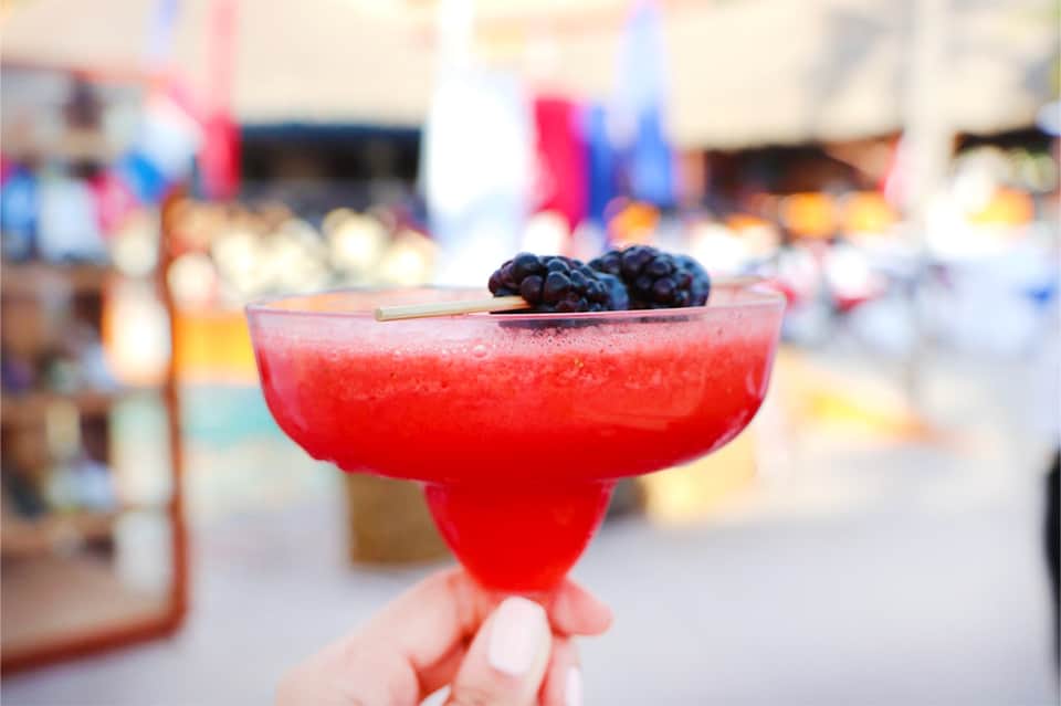 Colorful red cocktail garnished with blackberries held up against a blurred resort background